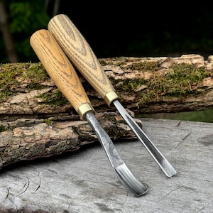 May include: Two wood carving gouges with light-colored, straight-grained wooden handles and brass ferrules. One tool features a curved metal blade, while the other has a straight, U-shaped metal gouge blade, both designed for woodworking tasks.