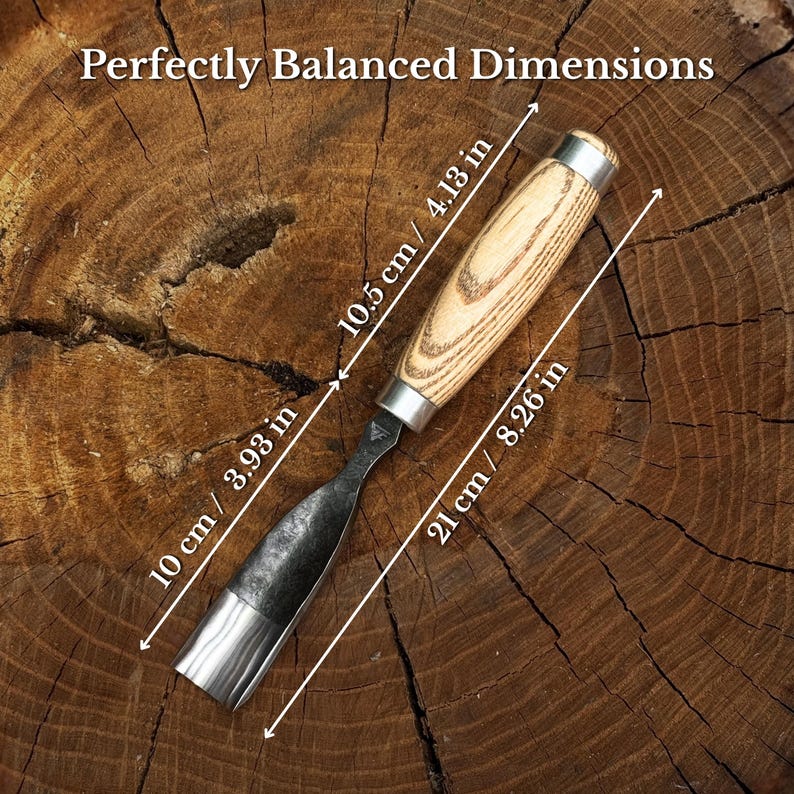 May include: A wood carving chisel with a light-coloured wooden handle and a dark metal blade. The tool features text stating Perfectly Balanced Dimensions and includes measurements of 10.5 cm / 4.13 in, 10 cm / 3.93 in, and 21 cm / 8.26 in.