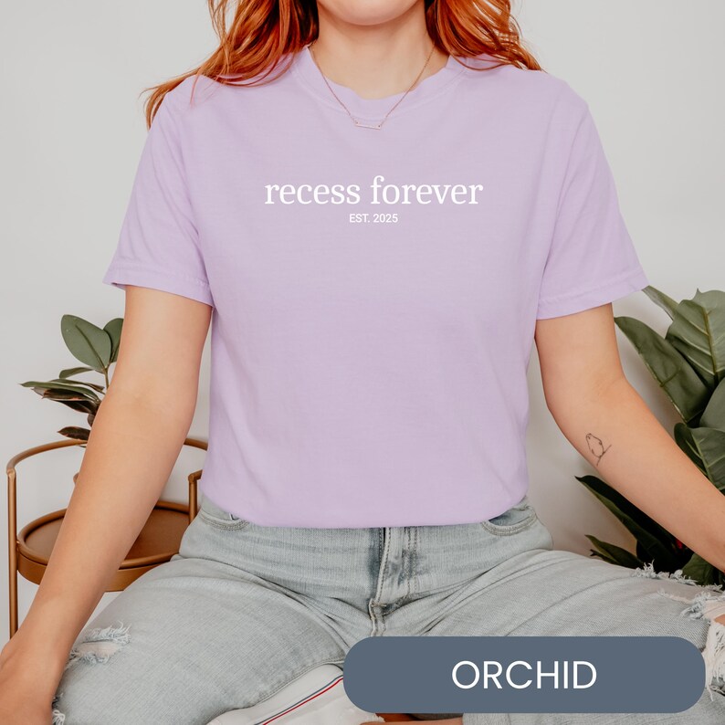 Op de afbeelding: Een lichtpaarse T-shirt met de tekst "recess forever est. 2025" in wit.