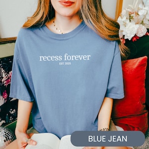 Op de afbeelding: Een jeansblauw t-shirt met de tekst "recess forever est. 2025" gedrukt op de voorkant.