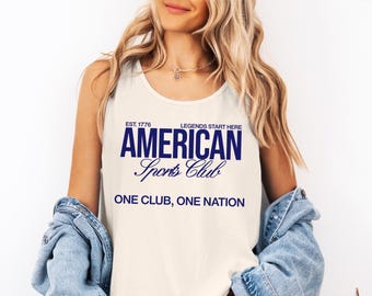 May include: Cream-colored tank top with the text "AMERICAN Sports Club" in navy blue. The text "EST. 1776" and "LEGENDS START HERE" are above the main text. Below the main text is "ONE CLUB, ONE NATION".