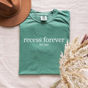 Op de afbeelding: Een turquoisegroen T-shirt met de tekst "recess forever" en "EST. 2025" in wit.