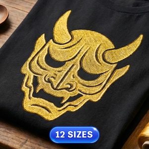 May include: Black t-shirt featuring a gold embroidered Oni mask design. The mask has horns and a fierce expression. The text "12 SIZES" is displayed in a blue oval at the bottom. The shirt is made of a soft material.