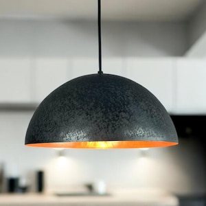 May include: A black dome-shaped pendant light fixture with a textured finish hangs from the ceiling in a kitchen. The light fixture has a warm, golden glow.