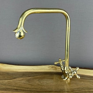 May include: A gold-toned kitchen faucet with a decorative spout and cross-shaped handles.