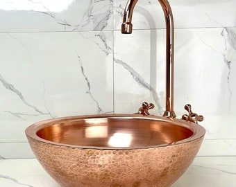 Könnte beinhalten: Ein gehämmertes Kupfer-Waschbecken mit einem passenden Kupferhahn. Das Waschbecken ist rund und hat eine gehämmerte Textur. Der Hahn hat einen einzigen Griff und einen Auslauf, der nach oben ragt.