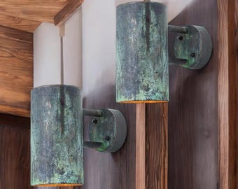May include: Two green metal wall sconces with a distressed finish. The sconces have a cylindrical shape and are mounted on a wall.