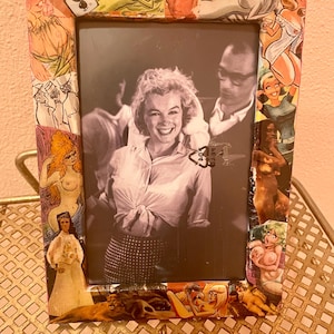 May include: A black and white photo of a couple dancing, framed in a picture frame covered in a collage of vintage pin-up images.