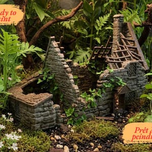 Peut inclure: Une miniature de ruine de chaumière en pierre, entourée de verdure et de mousse. La chaumière a un toit et des murs partiellement effondrés, avec le texte "Prêt à peindre" dans une bannière orange. Idéal pour les loisirs créatifs.