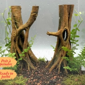 Op de afbeelding: Twee bruine boomstamdecoraties van hars met getextureerde schors en holle openingen, geplaatst in een glazen terrarium met donkere aarde, groen mos en kleine bladplanten. De tekst "Prêt à peindre" en "Ready to paint" is zichtbaar.