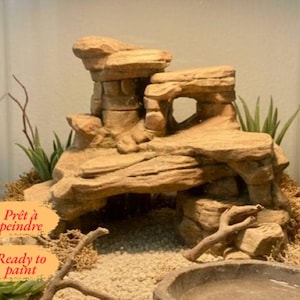 Op de afbeelding: Een beige, meerlaagse rotsformatie voor een terrarium met een holle boog, gestructureerde oppervlakken en gelaagde steendetails. De tekst "Prêt à peindre" en "Ready to paint" staat in het oranje gedrukt aan de linkeronderzijde.