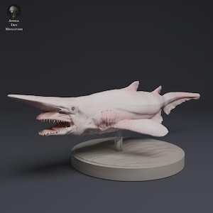 Puede incluir: Miniatura de tiburón duende de color rosa pálido, con un hocico largo y plano y dientes visibles. El modelo está montado sobre una base circular. El texto "Animal Den Miniatures" es visible.