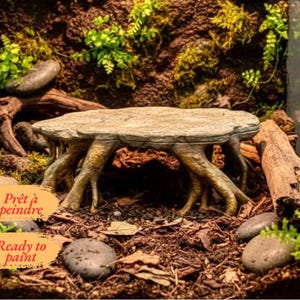 May include: A beige, textured, tree-stump-shaped platform with multiple root-like legs, featuring a flat, circular top surface. The object includes two orange labels with the text "Prêt à peindre" and "Ready to paint" printed in black.