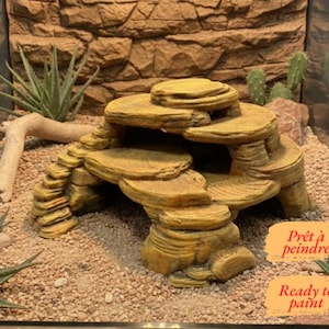 Könnte beinhalten: Ein beigefarbenes, mehrstufiges Felsversteck für Reptilien mit treppenartigem Design und hohlem Innenraum. Die Struktur weist eine texturierte Oberfläche auf, die an natürliche Sandsteinschichten erinnert. Der Text "Ready to paint" ist unten rechts.