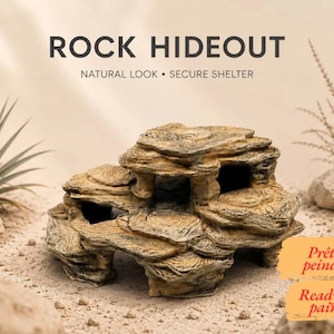 Puede incluir: Un escondite de roca en tonos beige y marrón con múltiples niveles y aberturas. El texto ROCK HIDEOUT, NATURAL LOOK • SECURE SHELTER, Prêt à peindre y Ready to paint es visible. La estructura tiene una superficie texturizada en capas.