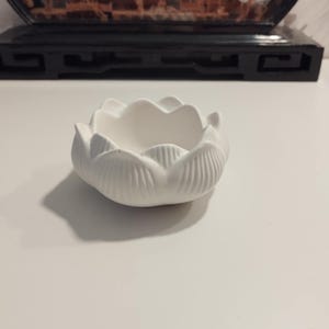 Könnte beinhalten: Weiße Keramik-Schale in Lotusblumenform. Die Schale hat eine glatte, abgerundete Oberfläche und einen leicht erhöhten Rand.