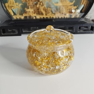 Może przedstawiać: Szklany słoik z pokrywką wypełniony złotymi i srebrnymi płatkami. Słoik ma okrągły kształt i gładką powierzchnię.