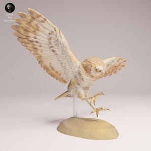 Può includere: Statuetta dettagliata di un gufo marrone chiaro con le ali spiegate, posato su una piccola base beige. Le piume del gufo sono finemente dettagliate con sfumature di marrone e bianco. Gli occhi gialli del gufo sono rivolti verso il basso.