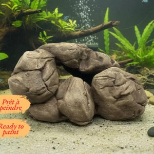 Peut inclure: Un ornement d'aquarium en forme de rocher texturé brun avec une ouverture centrale creuse. La surface présente des crevasses profondes et une finition mate. Deux étiquettes rectangulaires orange portent le texte "Prêt à peindre" et "Ready to paint".