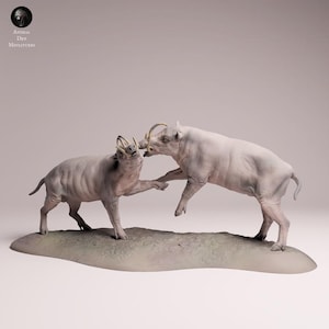 Peut inclure: Une sculpture détaillée de deux babiroussas de couleur claire dans une pose dynamique, semblant interagir. Les figurines ont des défenses proéminentes et sont posées sur une base texturée et terreuse. Le logo Animal Den Miniatures est dans le coin supérieur gauche.