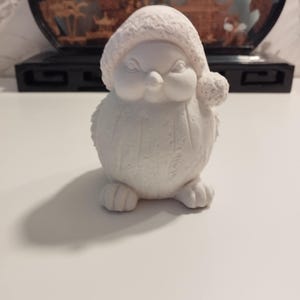 Peut inclure: Figurines d'oiseaux en céramique blanche portant un chapeau de Père Noël. L'oiseau a une surface texturée et est assis sur une surface blanche.