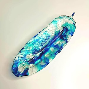 Può includere: Un piatto decorativo allungato in vetro a forma di piuma. Il piatto presenta un motivo a vortice di colori blu, turchese e bianco. Il piatto a forma di piuma è un oggetto di arredamento per la casa unico.