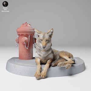 Op de afbeelding: Een handgeschilderd miniatuurbeeldje van een coyote die naast een rode brandkraan zit. De coyote ligt op een grijze betonnen basis.