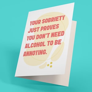 May include: A white greeting card with the text "YOUR SOBRIETY JUST PROVES YOU DON'T NEED ALCOHOL TO BE ANNOYING" in red letters. The text is inside a yellow and cream-colored design. The card is open, revealing a blank interior.
