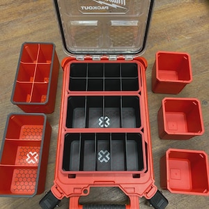 Könnte beinhalten: Roter und schwarzer Milwaukee Packout Werkzeugorganizer mit mehreren Fächern und herausnehmbaren Behältern. Das offene Gehäuse zeigt verschiedene Aufbewahrungsbereiche, einschließlich kleiner roter und schwarzer Behälter. Der Deckel ist transparent mit dem Milwaukee-Logo.