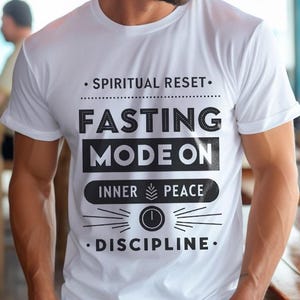 May include: White t-shirt with black text that reads "Spiritual Reset - Fasting Mode On - Inner Peace - Discipline". The text is stylized to look like a switch with the word "On" in a circle.