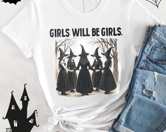 May include: White t-shirt featuring the text "GIRLS WILL BE GIRLS" above an illustration of six witches in black dresses and hats holding hands. The design is a Halloween theme.