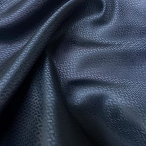Può includere: Un tessuto blu scuro con un sottile motivo geometrico in rilievo. Il tessuto ha una texture liscia e setosa.
