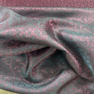 Puede incluir: Primer plano de una tela azul oscuro con un sutil patrón rosa y plateado. La tela tiene una textura suave y sedosa.