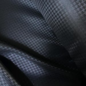 Può includere: Tessuto a pied-de-poule nero e bianco con un leggero luccichio. Il tessuto è piegato e drappeggiato, mostrando la trama e il motivo.