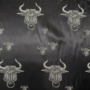 May include: Black fabric with a repeating pattern of silver bull heads. The bull heads have a ring in their noses.