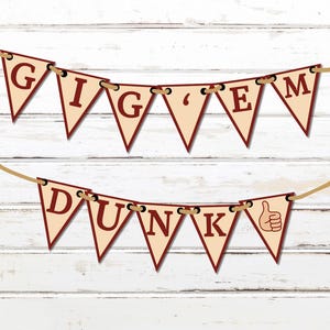 Puede incluir: Una pancarta triangular roja y blanca con las palabras "GIG 'EM DUNK" y un pulgar hacia arriba. La pancarta está enhebrada en una cuerda de hilo.