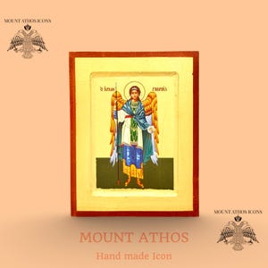 May include: Hand-made icon of an angel, framed in a gold-coloured wooden frame. The angel is depicted with a halo, holding a staff, and wearing a blue, white, and green robe. The text "Mount Athos" and "Hand made Icon" are at the bottom.