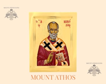 May include: Hand-painted icon of Saint Nicholas, also known as Santa Claus, with a red robe, black cross, and gold background. The icon is framed in gold and has Greek text on the top and bottom.