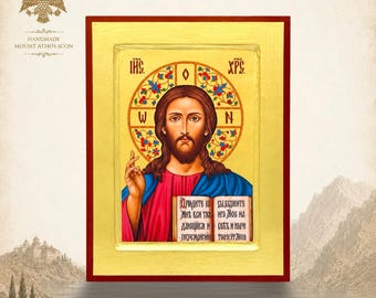 May include: A rectangular religious icon featuring a central figure of Jesus Christ with a brown beard and hair, wearing a red tunic and blue mantle. The figure holds an open book with Cyrillic text and has a gold halo with floral patterns.
