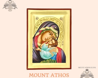 May include: Hand-painted icon of the Virgin Mary and baby Jesus. The icon is framed in a gold-coloured frame with a red border. The icon is set against a light pink background. The text "MOUNT ATHOS" is written in orange below the icon.