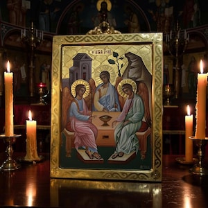 Könnte beinhalten: Eine rechteckige religiöse Ikone mit goldenem Rahmen, die drei geflügelte Gestalten an einem Tisch zeigt. Die Figuren tragen Gewänder in Rosa, Blau und Grün. Der griechische Text H AΓIA TPIA ist im oberen Bereich der Darstellung zu sehen.
