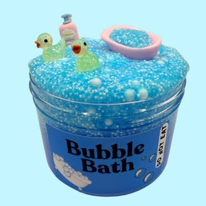 May include: Blue slime with white glitter and a bath tub, two rubber duckies, and a bottle of soap on top. The slime is in a clear jar with a blue label that says "Bubble Bath" and "Do Not Eat".