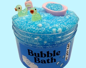 May include: Blue slime with white glitter and a bath tub, two rubber duckies, and a bottle of soap on top. The slime is in a clear jar with a blue label that says "Bubble Bath" and "Do Not Eat".