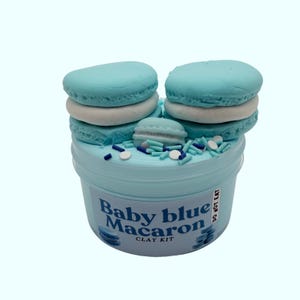 May include: A baby blue clay kit with a macaron theme. The kit includes a plastic container filled with blue clay, topped with blue and white macarons and sprinkles. The container has the text "Baby blue Macaron CLAY KIT".