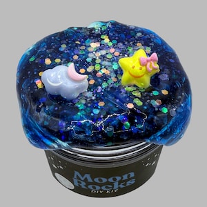 May include: Blue slime with glitter and a cloud, moon, and star charm. The slime is in a black jar with the label "Moon Rocks DIY Kit".