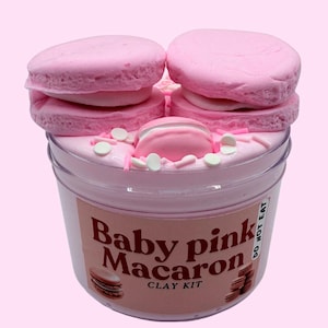 May include: A clear plastic pot filled with baby pink clay, decorated with pink macaron shapes and sprinkles. The label says "Baby pink Macaron CLAY KIT" with a macaron illustration. The words "DO NOT EAT" are also visible on the label.