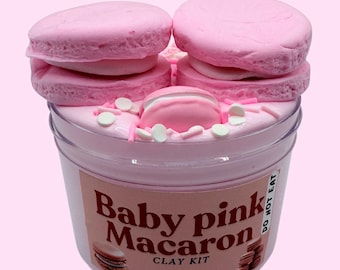 May include: A clear plastic container filled with baby pink-colored clay, topped with pink macaron-shaped decorations and sprinkles. The label reads "Baby pink Macaron CLAY KIT" with a macaron illustration. The words "DO NOT EAT" are also visible.