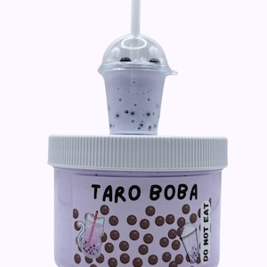 Lavender glossy slime in a clear jar labeled “Taro Boba,” topped with realistic ice cube charms, black boba ball charms, and a mini boba cup. Soft, thick texture and smooth finish, perfect for ASMR and bubble pops. Suitable for slime enthusiasts, collectors, and sensory play lovers.