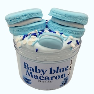 May include: A clear plastic pot filled with white slime, decorated with blue macarons and sprinkles. The label says "Baby blue Macaron CLAY KIT". The macarons are light blue with white filling. The sprinkles are blue and white.