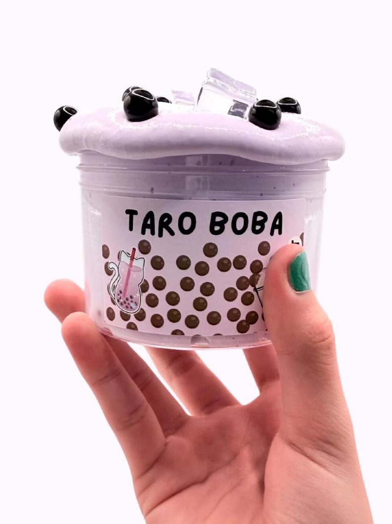 Lavender glossy slime in a clear jar labeled “Taro Boba,” topped with realistic ice cube charms, black boba ball charms, and a mini boba cup. Soft, thick texture and smooth finish, perfect for ASMR and bubble pops. Suitable for slime enthusiasts, collectors, and sensory play lovers.
